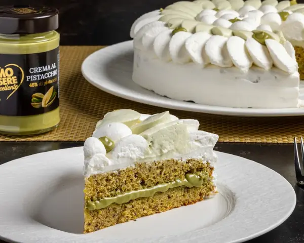 Una fetta di torta soffice al pistacchio, con crema al pistacchio e panna montata. Accanto, un barattolo di crema al pistacchio.