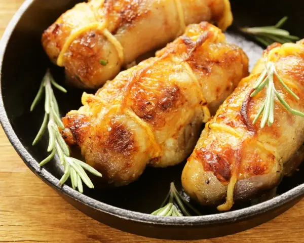 Involtini di pollo al forno dorati e succulenti, legati con spago da cucina e guarniti con rametti di rosmarino fresco, serviti in una padella di ghisa.