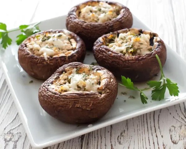 Quattro funghi ripieni al forno, dorati e invitanti, guarniti con prezzemolo fresco su un piatto bianco.