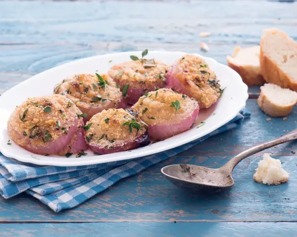 Deliziose cipolle al forno, dorate e profumate, servite su un piatto bianco con pane croccante e un cucchiaio d'argento.
