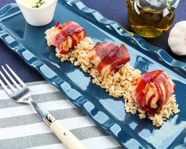 Tre bocconcini di pollo con pancetta avvolti e dorati, serviti su un letto di riso integrale.