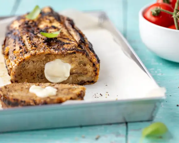 Polpettone di melanzane grigliato, ripieno di formaggio filante, su teglia con basilico e pomodorini.