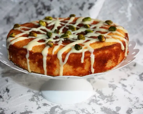 Deliziosa torta al bergamotto, decorata con glassa bianca e pistacchi croccanti, pronta per essere gustata.