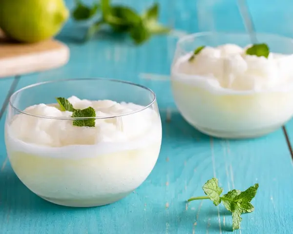 Sorbetto al limone senza gelatiera: due coppette di fresco sorbetto al limone guarnite con menta, su un tavolo di legno blu.