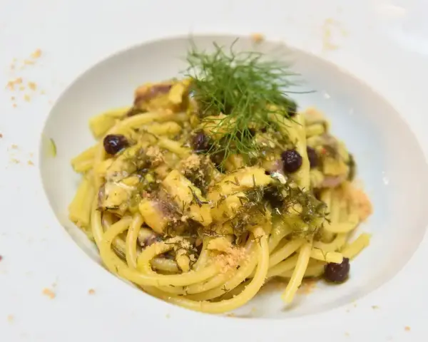 Un piatto invitante di pasta con finocchi, olive e acciughe, guarnito con erbe fresche e pangrattato.