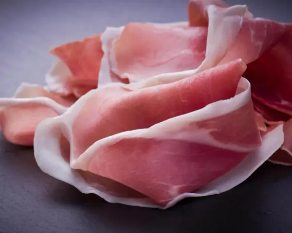 Fette di prosciutto crudo, un insaccato dal colore rosato e venature bianche, disposte su una superficie scura.