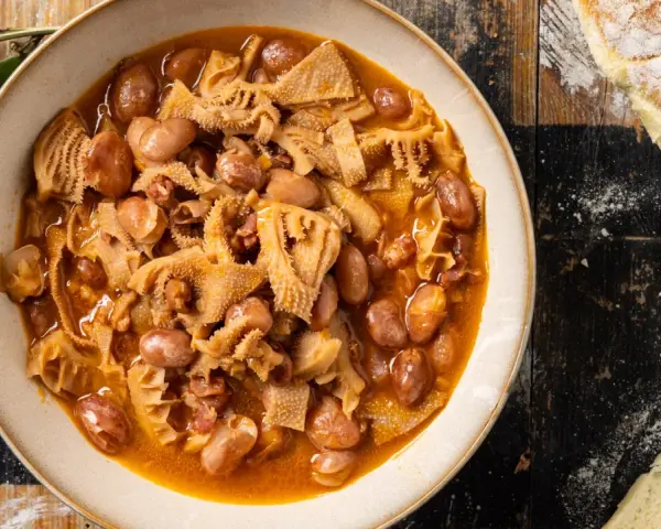 Piatto fumante di trippa alla milanese con fagioli, su un tavolo di legno rustico, accanto a pane casereccio.