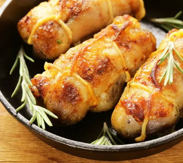 Involtini di pollo al forno dorati e succulenti, legati con spago da cucina e guarniti con rametti di rosmarino fresco, serviti in una padella di ghisa.