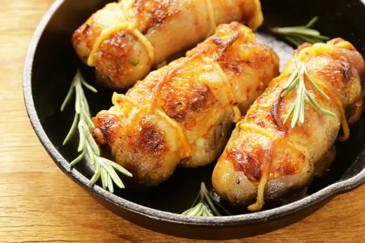 Involtini di pollo al forno dorati e succulenti, legati con spago da cucina e guarniti con rametti di rosmarino fresco, serviti in una padella di ghisa.