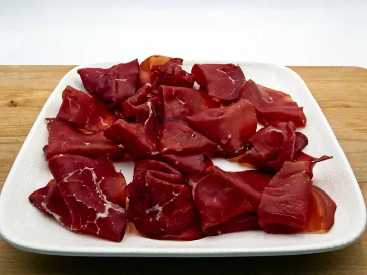Fetta di bresaola scura, forse di cavallo, su un piatto bianco. Meglio bresaola di cavallo o manzo? La scelta è tua!