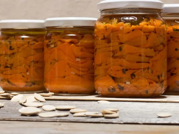 Barattoli di zucca sott'olio in agrodolce, con semi di zucca sparsi sul tavolo di legno.