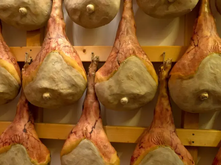 Filetti di salumi appesi a stagionare su scaffali di legno.