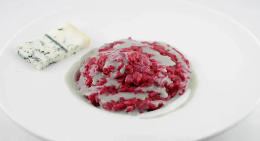 Risotto barbabietola e gorgonzola, un piatto vibrante e saporito, con una fetta di formaggio blu accanto.