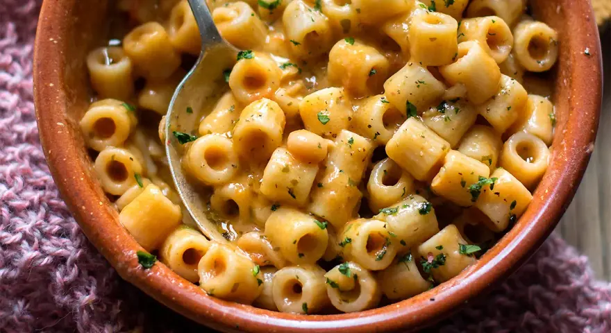 Una ciotola di terracotta piena di pasta e fagioli saporita, con un cucchiaio che ne raccoglie una porzione.