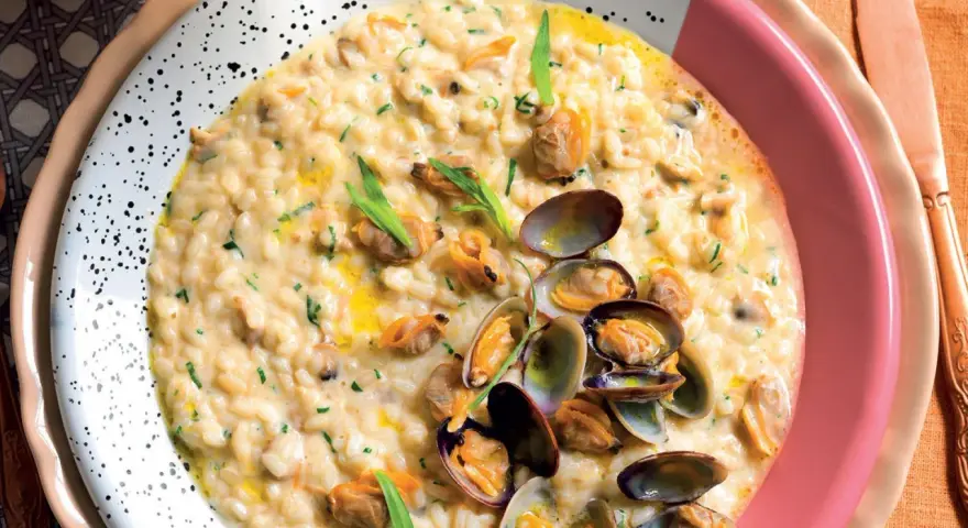 Un cremoso risotto alle vongole, guarnito con prezzemolo tritato e cozze fresche, servito in un piatto bianco a pois.