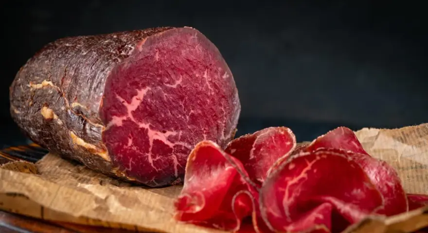 Un pezzo intero e fette sottili di bresaola, con la sua carne rossa e marezzata, evidenziano la differenza tra bresaola e punta d'anca.