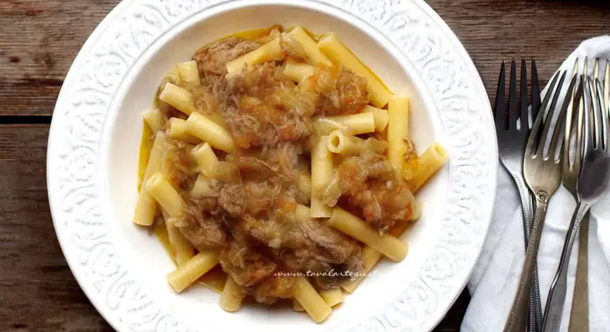 Piatto di pasta con ragù genovese napoletana, servito in un piatto bianco decorato, con forchette d'argento accanto.