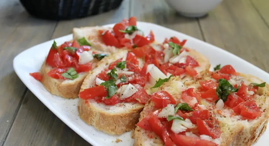 Fette di pane tostato condite con pomodoro fresco, cipolla e basilico, un classico della panzanella romana.
