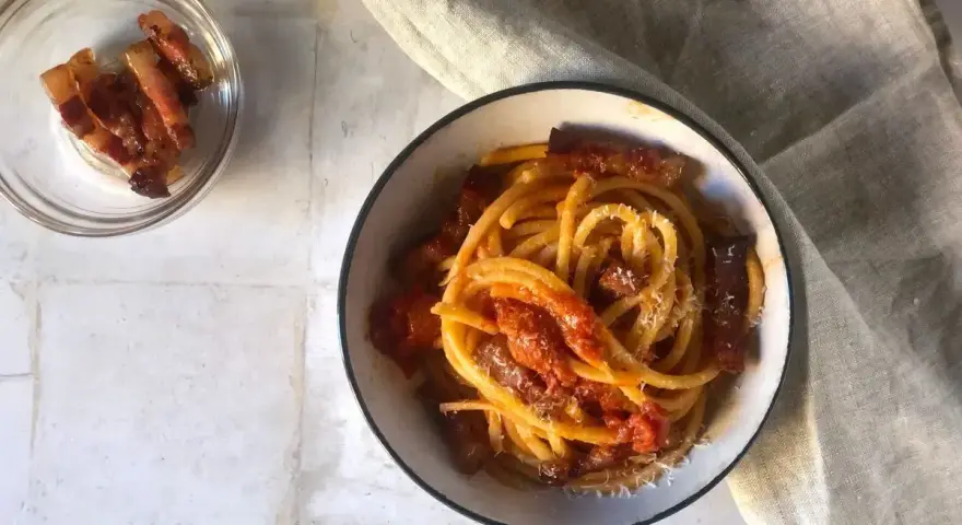 Un piatto invitante di bucatini all'amatriciana, con guanciale croccante e una salsa rossa saporita, spolverato di formaggio grattugiato.