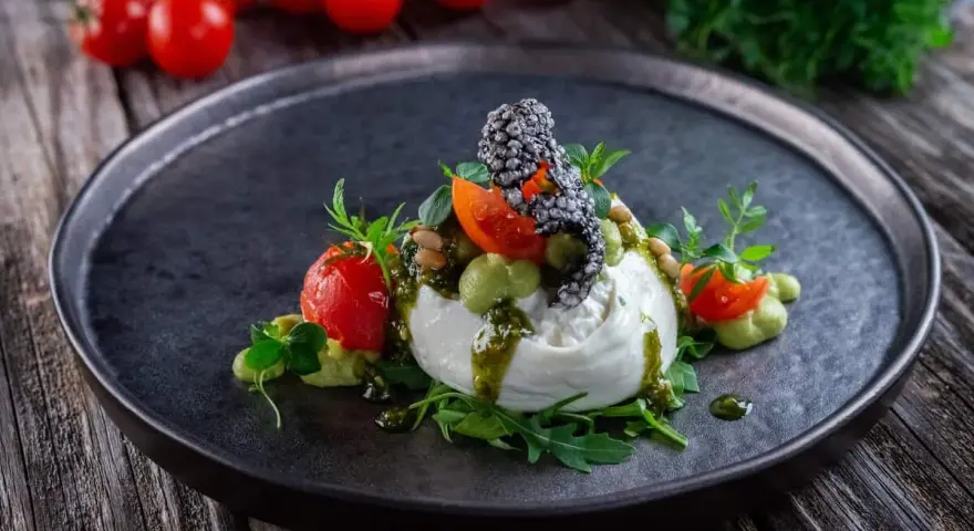 Burrata affumicata con pomodorini, crema di piselli, pinoli e pesto. Un piatto che esalta gli abbinamenti perfetti.