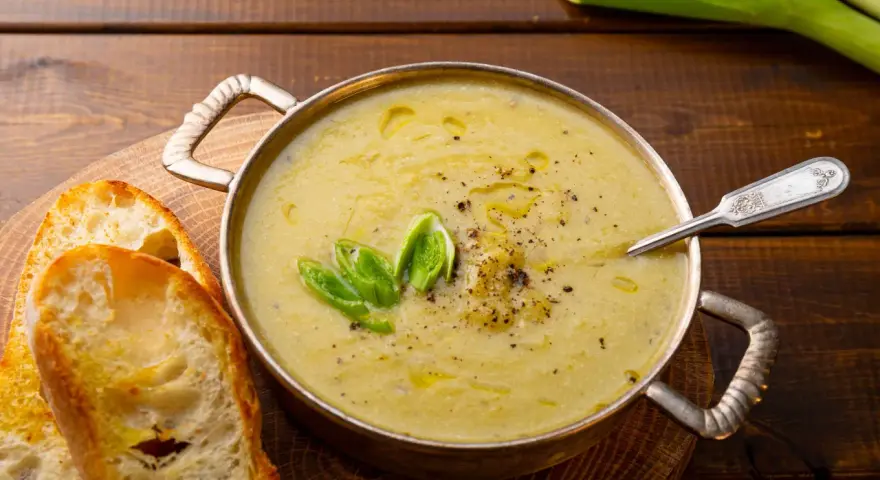 Una ciotola di calda crema di patate, guarnita con erba cipollina e pepe, servita con fette di pane tostato.