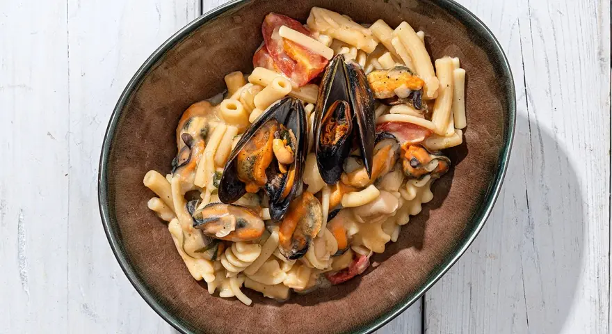 Piatto di pasta con fagioli e cozze, condita con pomodorini e una cremosa salsa.
