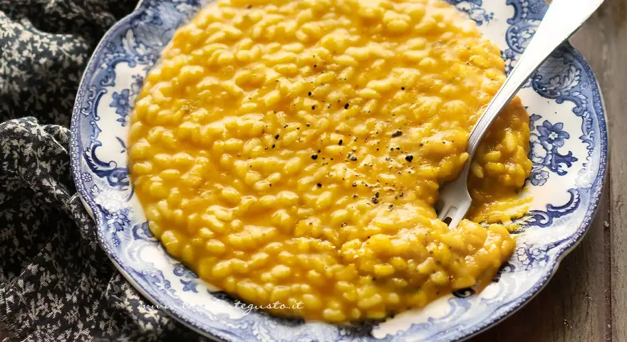 Un cremoso risotto con la zucca, servito su un piatto decorato con un motivo blu e bianco. Un cucchiaio d'argento è immerso nel piatto.