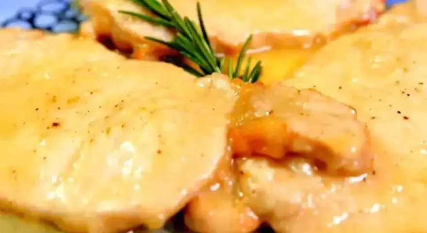 Deliziose scaloppine di maiale in salsa dorata, guarnite con un rametto di rosmarino fresco.