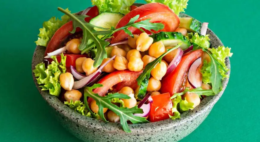 Insalata di ceci colorata con pomodori, cetrioli, cipolla rossa, lattuga e rucola in una ciotola grigia.