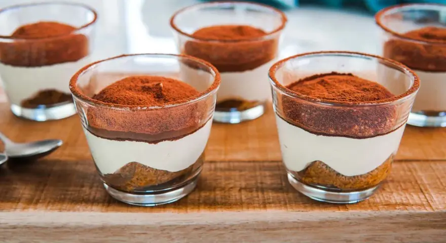 Delizioso tiramisù con pavesini senza uova, servito in bicchierini trasparenti e spolverato di cacao.