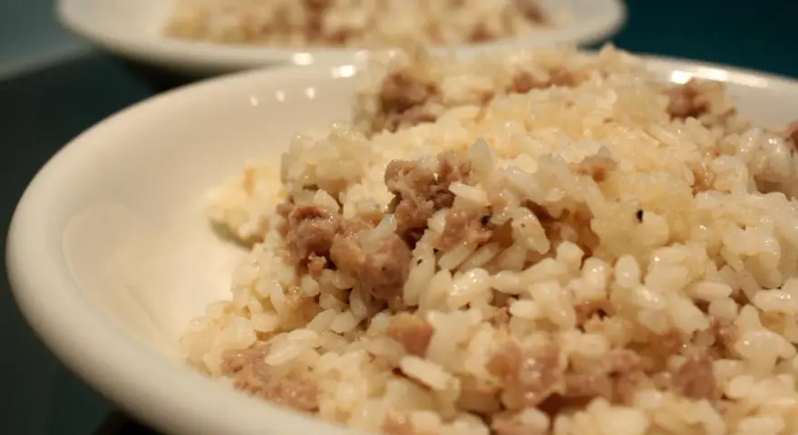 Risotto alla mantovana ingredienti: riso cremoso con salsiccia sbriciolata, servito in una ciotola bianca.