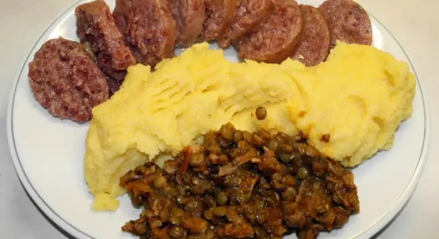 Piatto con fette di cotechino o musetto, polenta gialla e lenticchie stufate.