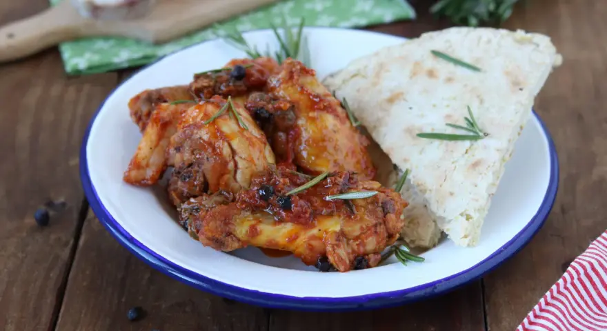 Piatto di friccò di pollo con pomodoro, olive e rosmarino, accompagnato da pane rustico.