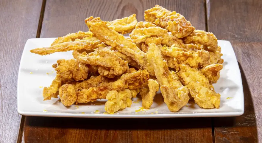 Un mucchio di croccante trippa fritta dorata, cosparsa di scorza di limone, su un piatto bianco.