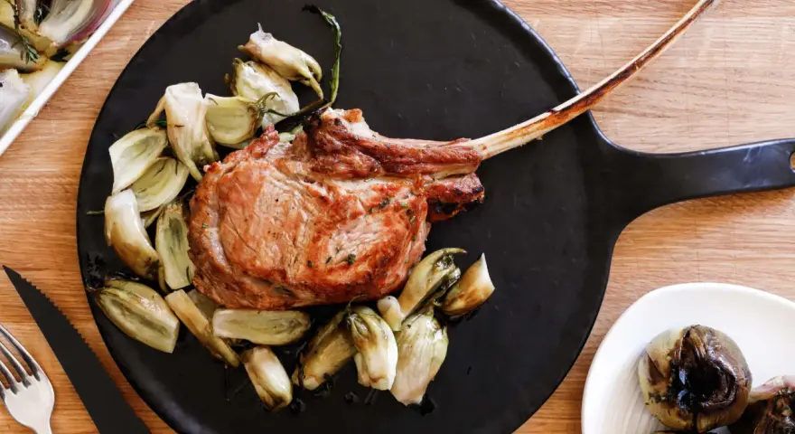 Un succulento tomahawk alla griglia, servito con verdure arrosto su un piatto nero.