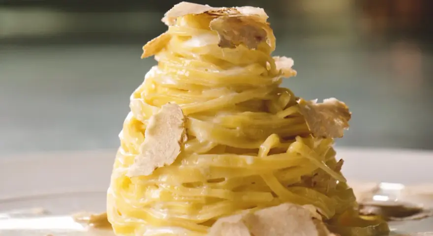 Un nido di pasta al tartufo, condita con una cremosa salsa e guarnita con scaglie sottili di tartufo bianco.