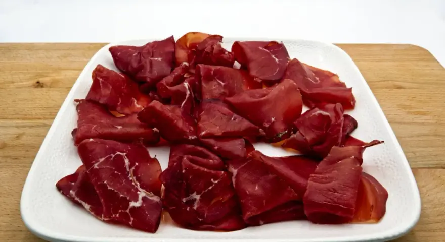 Fetta di bresaola scura, forse di cavallo, su un piatto bianco. Meglio bresaola di cavallo o manzo? La scelta è tua!