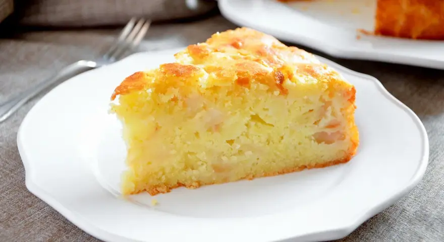 Una fetta di torta margherita con mele, soffice e dorata, servita su un piatto bianco.
