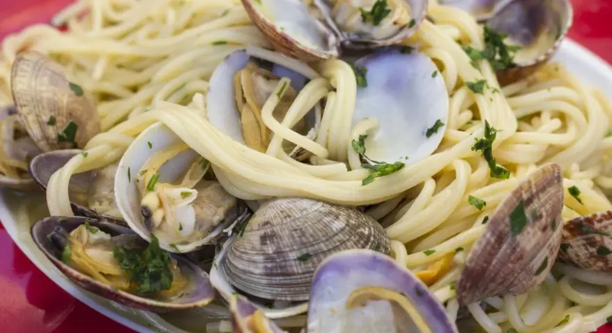 Un piatto invitante di spaghetti alle vongole, con pasta dorata e molluschi freschi guarniti da prezzemolo tritato.