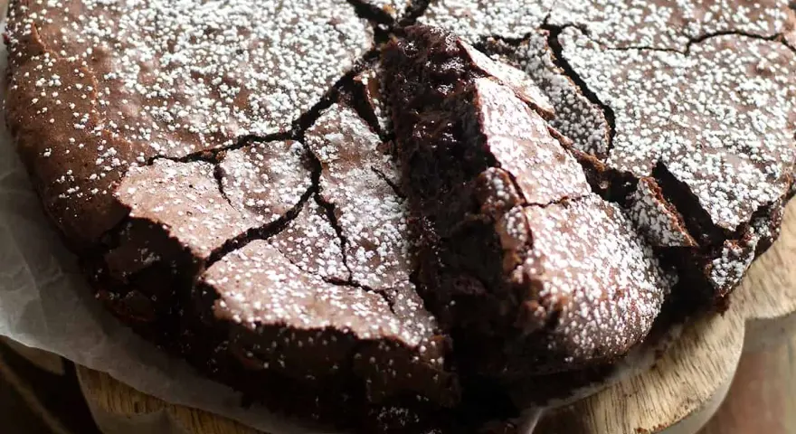 Torta fondente al cioccolato, con una crosta screpolata e cosparsa di zucchero a velo, pronta per essere gustata.