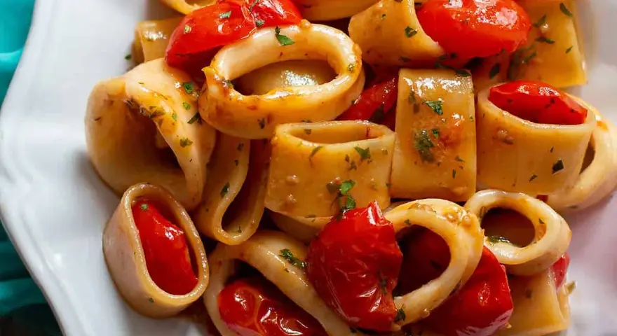Un piatto invitante di pasta calamarata con pomodorini freschi e prezzemolo tritato, pronto per essere gustato.