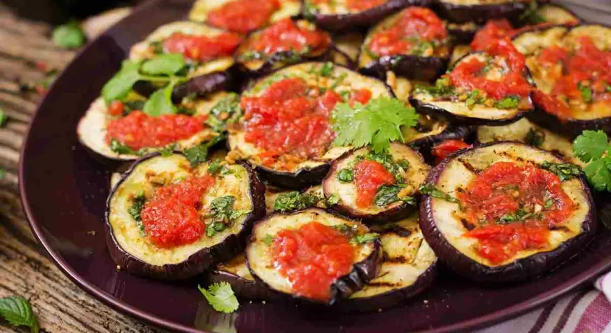 Fette di melanzane grigliate condite con salsa di pomodoro e basilico, un piatto gustoso di melanzane alla pizzaiola.