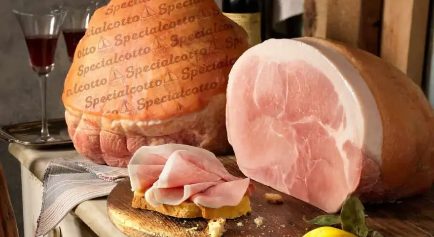 Due prosciutti, uno intero e uno affettato su pane, con una bottiglia di vino e un limone. Il cotto prosciutto è pronto per essere gustato.