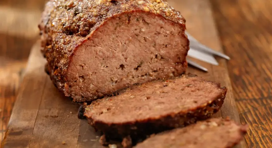 Un succulento polpettone al forno, tagliato a fette su un tagliere di legno, pronto per essere gustato.