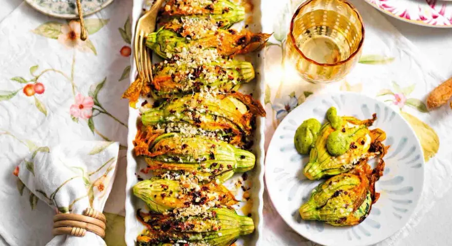 Deliziosi fiori di zucca ripieni, dorati e croccanti, serviti su un piatto con un tocco di verde.