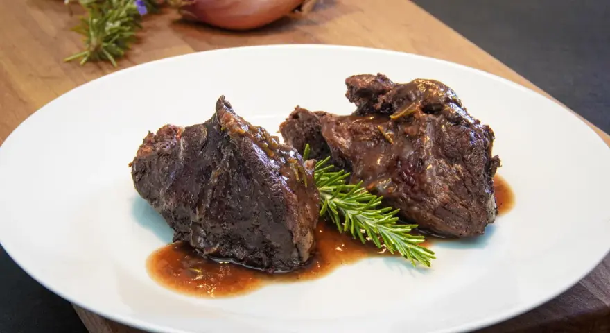 Guancia di manzo brasata, tenera e succulenta, servita su un piatto bianco con rosmarino fresco. Un piatto che fa chiedere: guancia di manzo cos'è?
