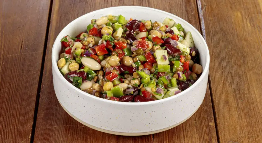 Una ciotola piena di colorata insalata di legumi, con ceci, fagioli, lenticchie, peperoni, cipolla rossa e prezzemolo fresco.