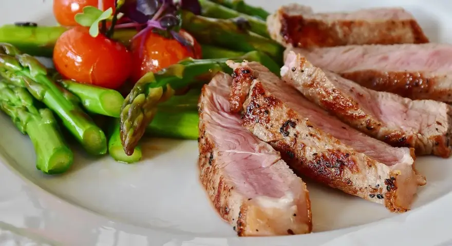 Fette di manzo magro cos'è? Succulenta carne con asparagi verdi e pomodorini su un piatto bianco.