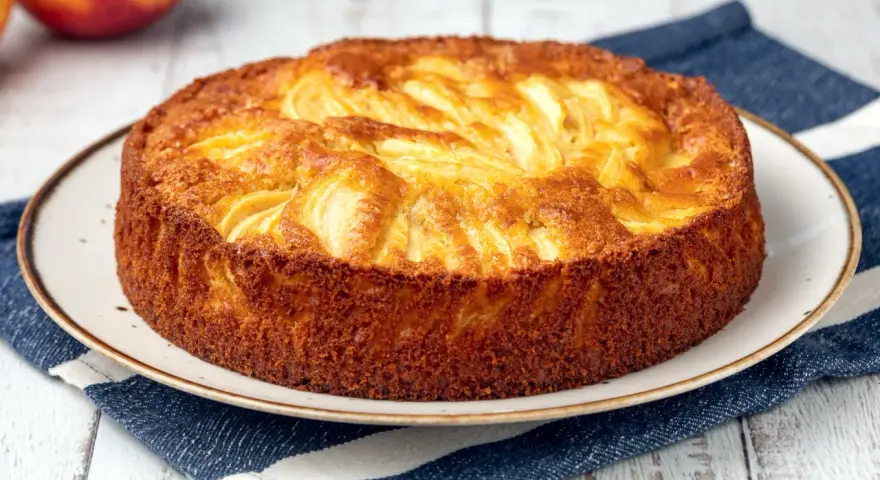 Torta di mele dorata, appena sfornata, con mele a vista. Perfetta da spennellare con un po' di sciroppo.