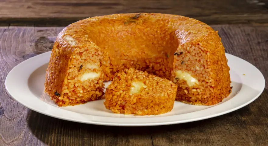 Un invitante timballo di riso, dorato e ripieno di formaggio filante, pronto per essere gustato su un piatto bianco.